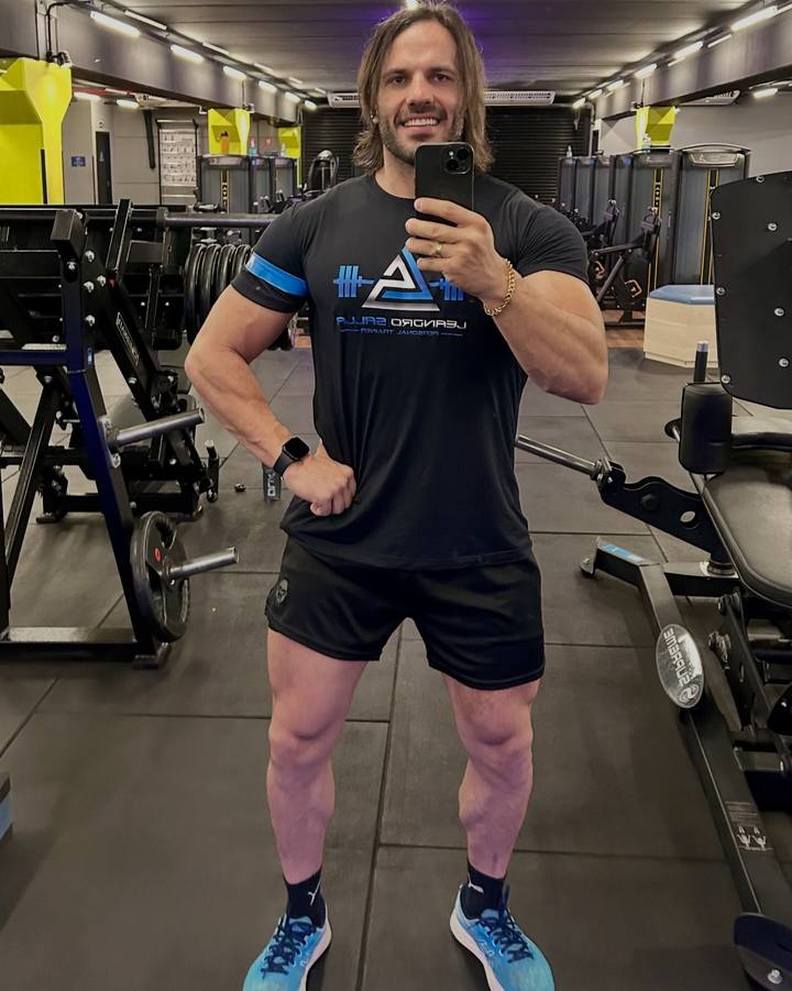 Leandro Salla na academia com o celular na mão, com a camiseta da sua marca